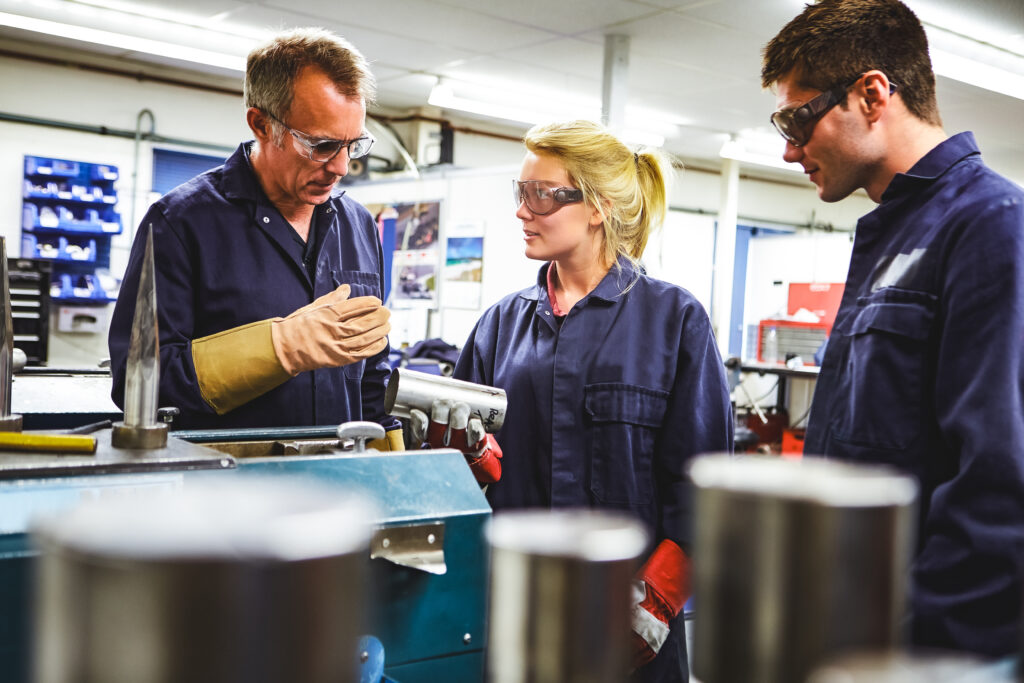 Engineer Working With Apprentices On Factory Floor