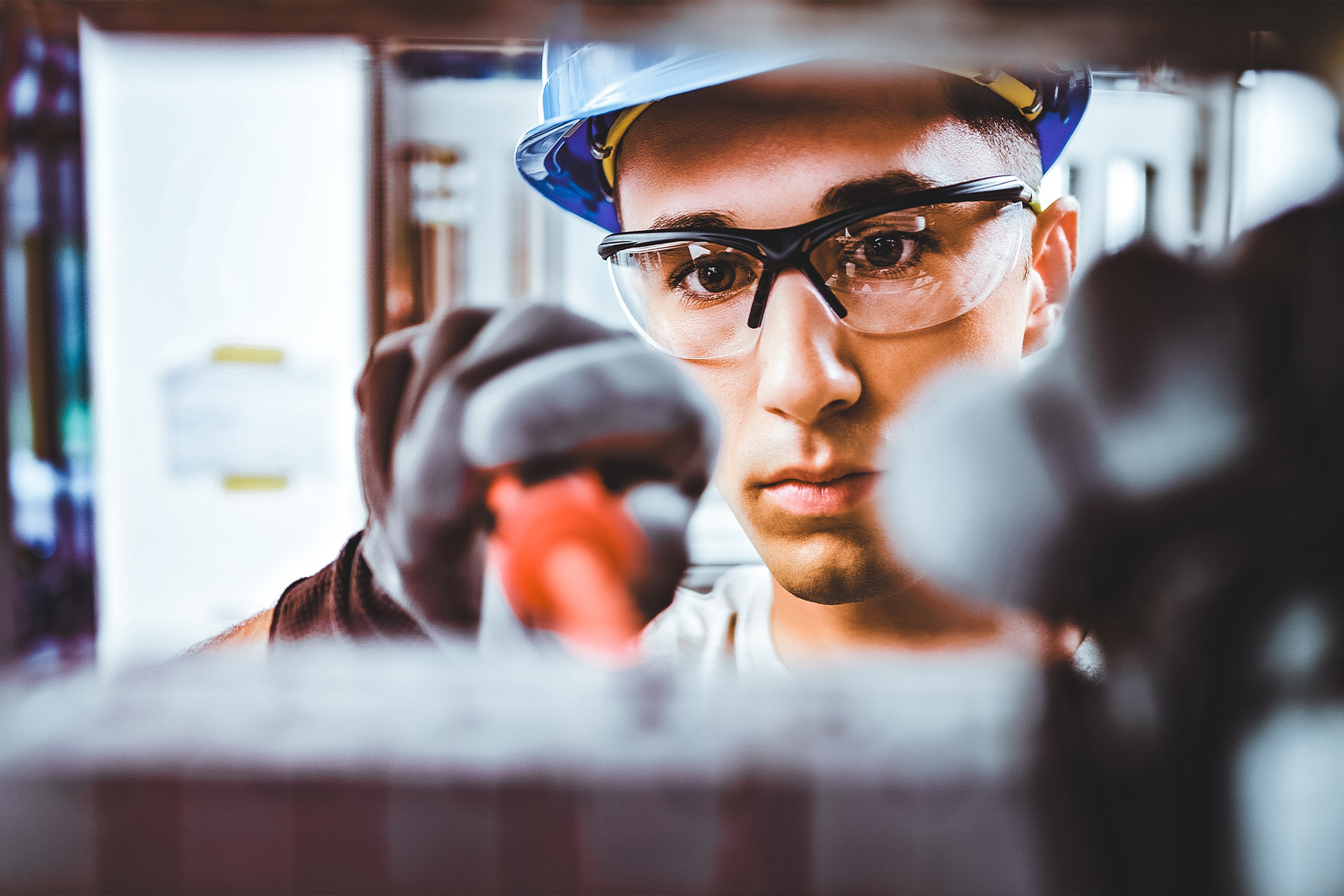 young man with safety glasses and a hard hat using a screwdriver