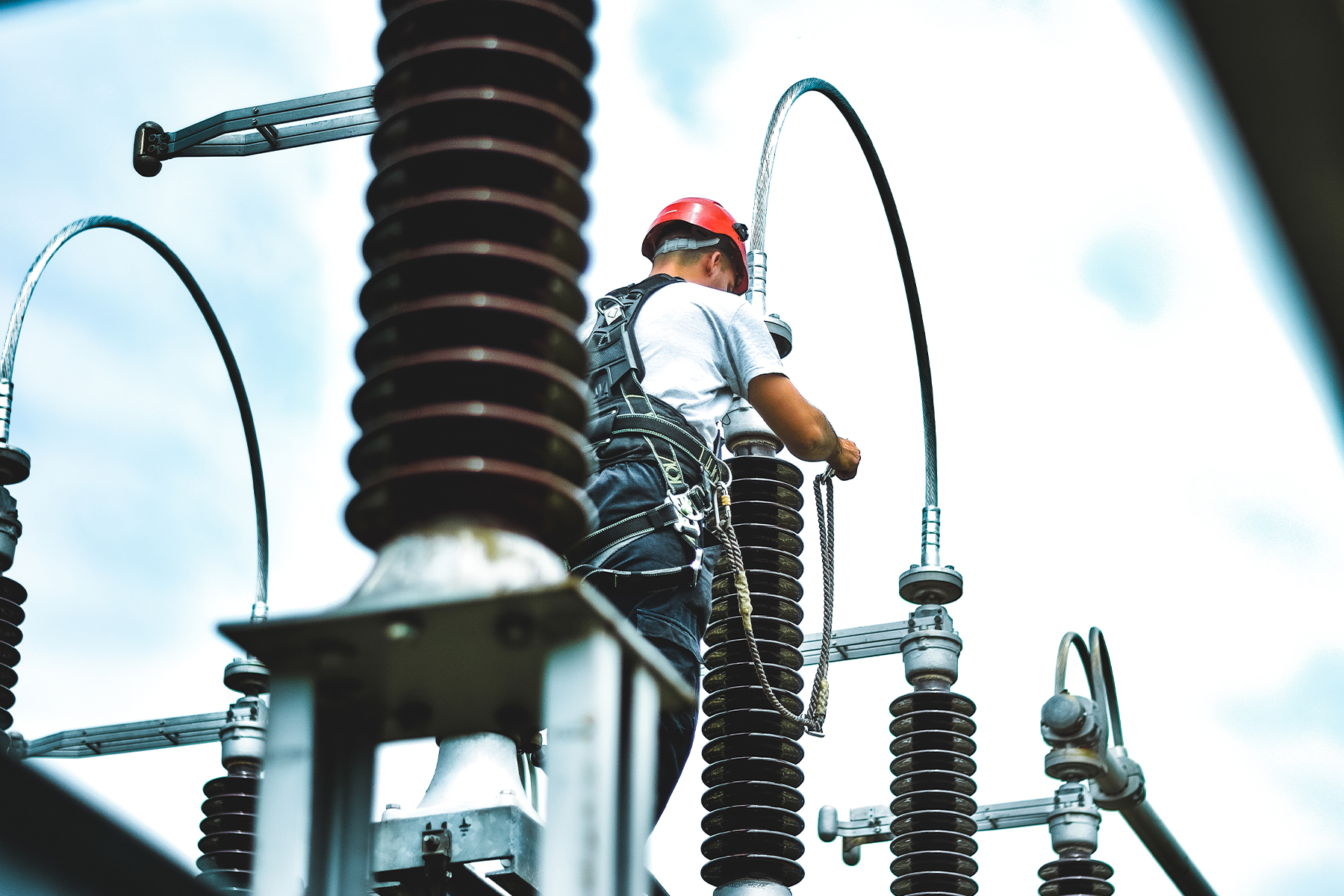 A man in a safety hat and safety harness working in an electrical substation