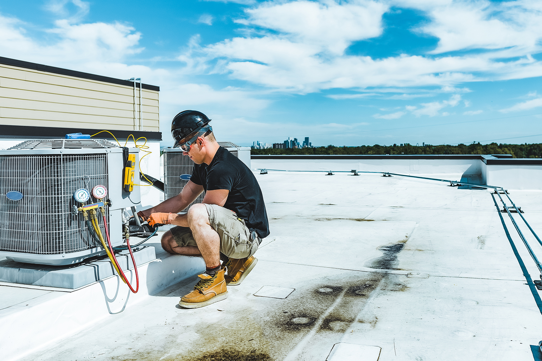 a young man in a hard hat and safety googles working on a rooftop hvac unit