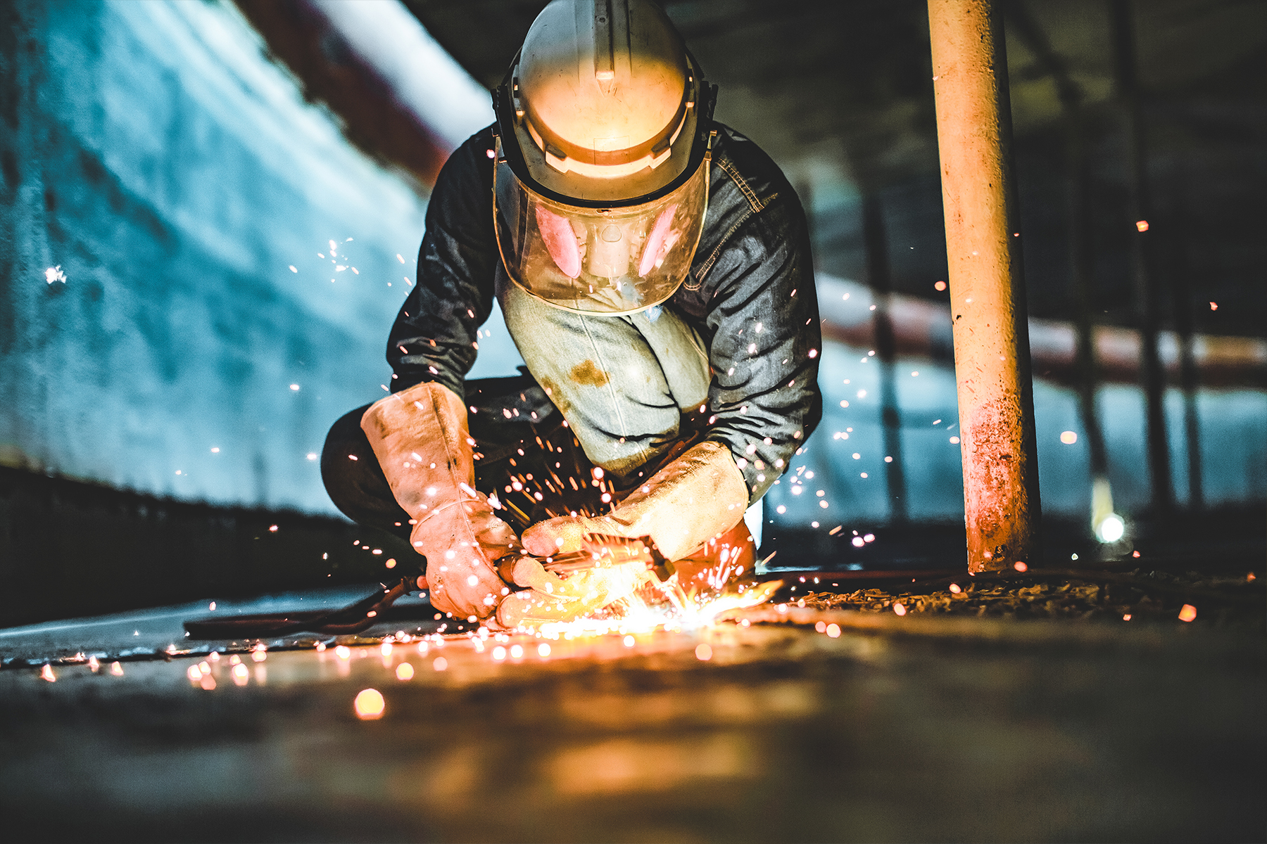 a person in a welding helmet and gloves welds a large piece of sheetmetal with sparks flying